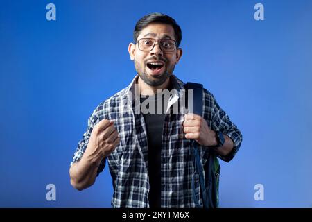Nahaufnahme eines gutaussehenden Studenten, der einen Rucksack trägt und mit blauem Hintergrund lächelt. Stockfoto