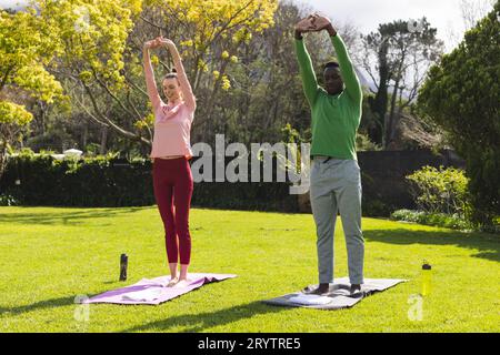 Glückliches, vielseitiges Paar, das Yoga und Dehnen im Garten praktiziert Stockfoto