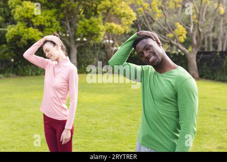 Glückliches, vielseitiges Paar, das Yoga und Dehnen im Garten praktiziert Stockfoto