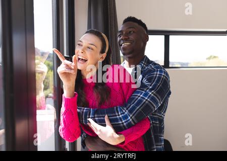 Glückliches, vielseitiges Paar, das zu Hause durch das Fenster schaut Stockfoto