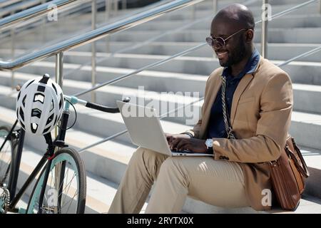 Junger afroamerikanischer Solopreneur oder Freelancer, der auf der Laptop-Tastatur sitzt und im Chat kommuniziert Stockfoto