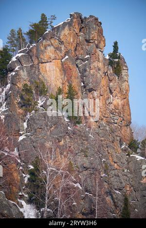 Felsiger Berg bedeckt mit Wald und Schnee vor dem blauen Himmel. Stockfoto