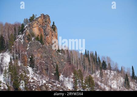 Felsiger Berg bedeckt mit Wald und Schnee vor dem blauen Himmel. Stockfoto