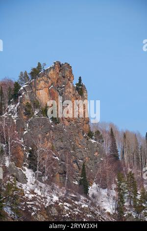 Felsiger Berg bedeckt mit Wald und Schnee vor dem blauen Himmel. Stockfoto