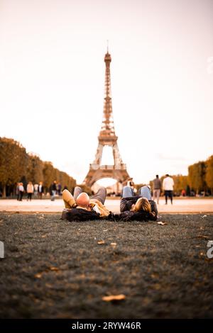 Ein junges erwachsenes Paar, das einen romantischen Moment zusammen genießt, während es vor dem berühmten Eiffelturm in Paris, Frankreich, auf dem Boden liegt Stockfoto