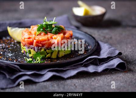 Roher Lachs, Avocado purple Zwiebel Salat serviert kulinarische Ring auf schwarze Platte. Schwarz konkreten Hintergrund Stockfoto