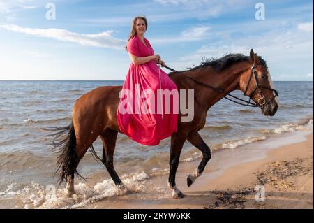 Eine attraktive junge Frau genießt eine gemütliche Fahrt auf einem schönen Pferd an einem atemberaubenden Strand Stockfoto