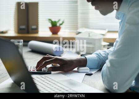 Konzentrieren Sie sich auf die Hand eines jungen männlichen Architekten, der die Tasten des Rechners drückt, während er am Arbeitsplatz im Büro sitzt und technische Berechnungen macht Stockfoto