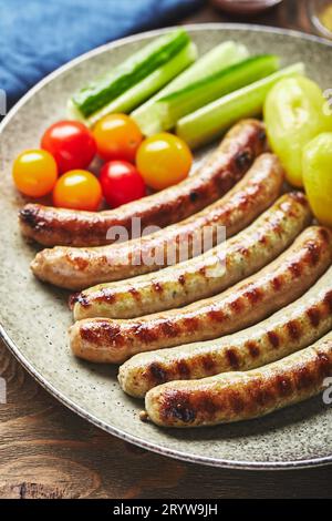 Vorzügliche gegrillte Würstchen mit Kartoffeln und Gemüse auf Teller in einer Nahaufnahme auf hölzernem Hintergrund. Draufsicht, flach. Stockfoto