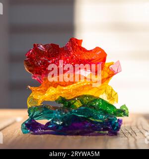 Regenbogenhaufen aus farbigen süßen Plastikverpackungen – rot, orange, gelb, grün, türkisblau, violett – auf Holzoberfläche, vor einem glatten Hintergrund. Stockfoto
