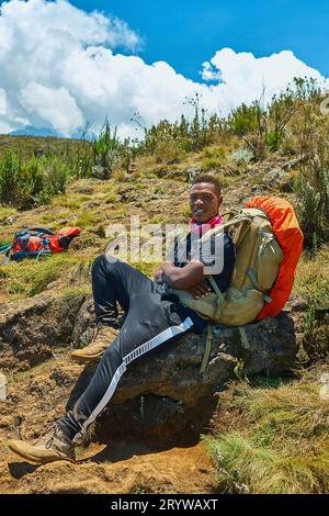 Ein dunkelhäutiger Kerl mit Rucksack ruht in den Bergen Stockfoto