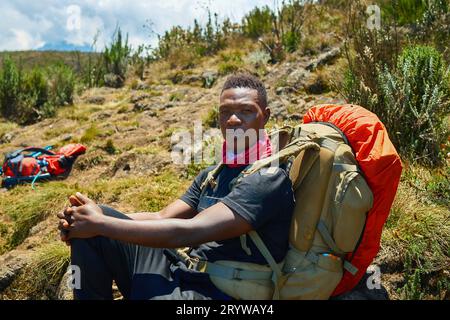 Ein dunkelhäutiger Kerl mit Rucksack ruht in den Bergen Stockfoto