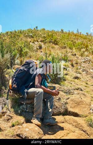 Ein dunkelhäutiger Kerl mit Rucksack ruht in den Bergen Stockfoto