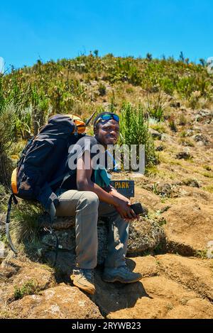 Ein dunkelhäutiger Kerl mit Rucksack ruht in den Bergen Stockfoto