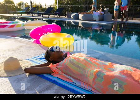Glückliche afroamerikanische Frau, die auf Handtuch liegt und sich neben dem Swimmingpool im Garten sonnt Stockfoto