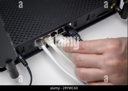 Eine Nahaufnahme einer Person, die Kabel an einen Router angeschlossen hat. Eine Person stellt über ein RJ45-Kabel eine Verbindung zu einem WLAN-Router her. Stockfoto