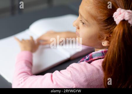 Erhöhter Blick auf blindes, birassisches Schulmädchen am Schreibtisch, das brailleschrift im Unterricht liest Stockfoto