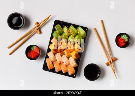 Ein Set von hellen mehrfarbigen Sushi-Rollen mit Garnelen, Lachs, Avocado in Plastikverpackung, chinesischen Essstäbchen, Soße, Ingwer auf weißem Hintergrund Stockfoto