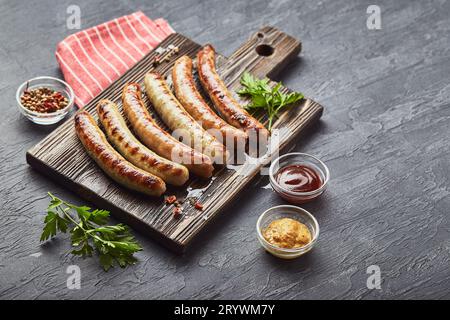 Leckere gegrillte Schweinefleischwürste mit Gewürzen und Kräutern auf hölzernem Schneidebrett aus nächster Nähe. Stockfoto