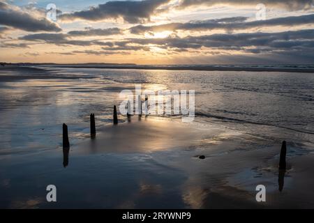 Eine Reihe von Polen am Strand, die unter einem dramatischen Sonnenuntergang ins Meer führt Stockfoto