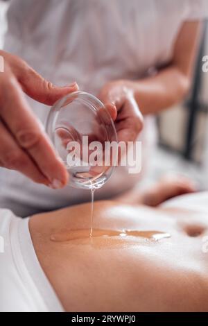 Crop gesichtslose Masseuse Gießen Öl auf die Hand während der entspannenden Massage Im Spa-Center Stockfoto