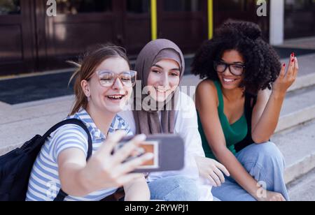 Drei süße Teenager-Mädchen verschiedener Nationalitäten machen ein Selfie. Kaukasische, afro-amerikanische und muslimische Teenagerinnen nehmen einen Tag Stockfoto