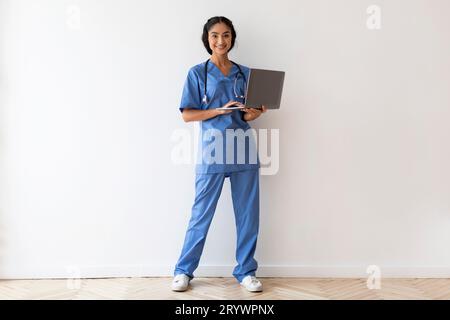 Gesundheitswesen Und Telemedizin. Lächelnde Indische Ärztin Trägt Uniform Und Hält Laptop Stockfoto