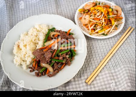 Rindfleisch in Scheiben mit grünen Bohnen und Reis, Mangosalat mit Garnelen, Essstäbchen. Vietnamesische Mahlzeit. Stockfoto