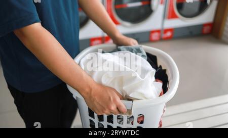 Hausmann mit Korb und schmutziger laundryÂ gewaschener Kleidung im Waschraum. Waschen machineÂ im Wäschereigeschäft Stockfoto