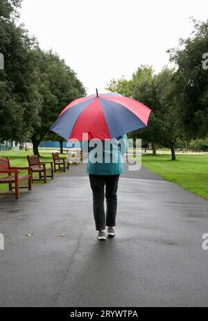 Eine Dame, die durch den Park schlendert, während eines plötzlichen Regenschauers Stockfoto