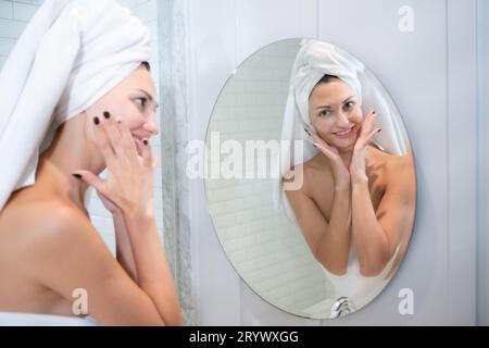 Junge schöne Frau, die vor dem Spiegel Creme auf ihr Gesicht aufträgt Stockfoto
