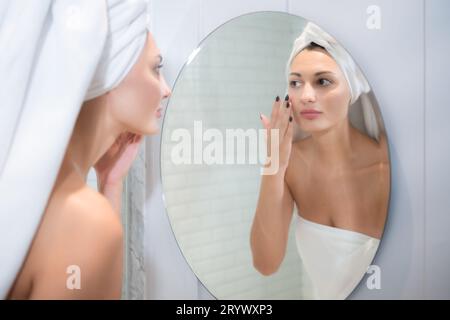 Junge schöne Frau, die vor dem Spiegel Creme auf ihr Gesicht aufträgt Stockfoto