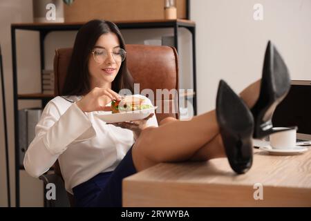 Junge Geschäftsfrau mit leckerem Sandwich im Büro Stockfoto