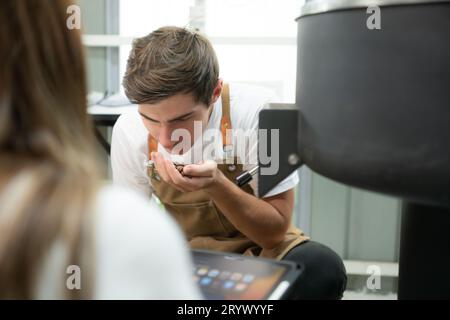 Junger Mann und Frau, die in der Kaffeebohnenröstung arbeiten, überprüfen die gerösteten Kaffeebohnen. Stockfoto