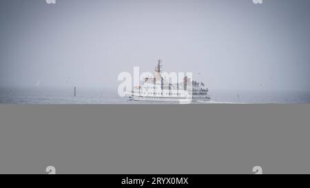 02.10.2023 Bensersiel, Esens, Ostfriesland, Niedersachsen, Deutschland - Insel Fähre vor dem Strand mit Strandkörbe und Menschen mit Bollerwagen - Symbolbild Nordsee, Urlaub, Wattenmeer, Herbst, Friesland *** 02 10 2023 Bensersiel, Esens, Ostfriesland, Niedersachsen, Deutschland Inselfähre vor dem Strand mit Liegestühlen und Menschen mit Trolleysymbol Bild Nordsee, Urlaub, Wattenmeer, Herbst, Frisia Credit: Imago/Alamy Live News Stockfoto