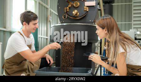 Junger Mann und Frau, die in der Kaffeebohnenröstung arbeiten, überprüfen die gerösteten Kaffeebohnen. Stockfoto