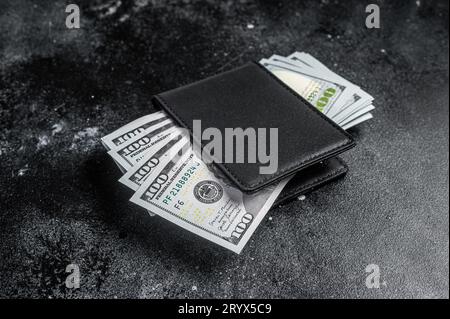 Eine schwarze Handtasche mit dem großen Päckchen Dollar, Bargeld-Schein. Schwarzer Hintergrund. Draufsicht. Speicherplatz kopieren. Stockfoto