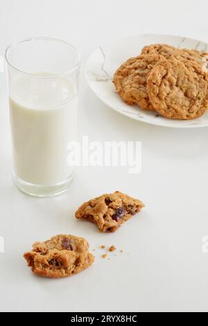 Haferflocken, Rosinen- und Walnusskekse mit hohem Glas Milch auf weißem Hintergrund im vertikalen Format. Selektive Fokussierung auf das vordere Stück des Kekses. Stockfoto