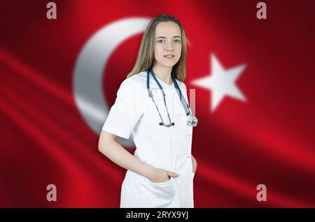 Eine junge Ärztin in einem weißen Mantel und einem Stethoskop steht auf dem Hintergrund der Flagge der Türkei. Stockfoto