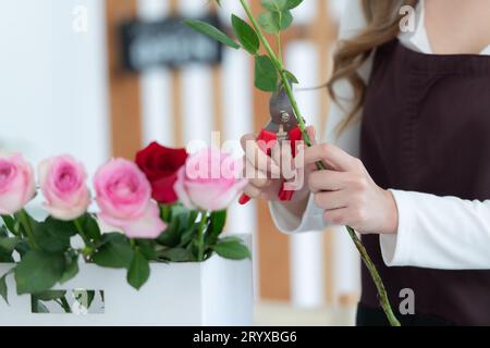 Schöne junge asiatische Floristin schneidet Rosenblume im Blumenladen Stockfoto