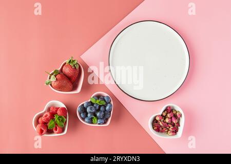 Leerer Teller und kleine Teller in Form von Herzen mit frischen Erdbeeren, Himbeeren, Heidelbeeren auf rosafarbenem Hintergrund. Obere V Stockfoto