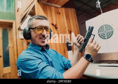Ein Mann übt das Schießen mit einer Pistole auf einem Schießstand, während er schützende Kopfhörer trägt Stockfoto