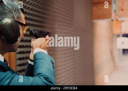 Ein Mann übt das Schießen mit einer Pistole auf einem Schießstand, während er schützende Kopfhörer trägt Stockfoto