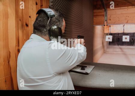 Ein Mann übt das Schießen mit einer Pistole auf einem Schießstand, während er schützende Kopfhörer trägt Stockfoto