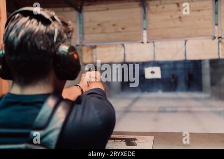 Ein Mann übt das Schießen mit einer Pistole auf einem Schießstand, während er schützende Kopfhörer trägt Stockfoto