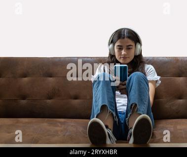 Mädchen, das auf dem Sofa sitzt und ein Mobiltelefon mit Kopfhörern benutzt Stockfoto