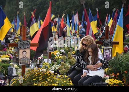 Lviv, Ukraine. Oktober 2023. Eine Frau und ein Kind sitzen in der Nähe des Grabes eines ukrainischen Soldaten, der während des russisch-ukrainischen Krieges auf dem Lychakiv-Friedhof in Lemberg am Tag des Verteidigers der Ukraine getötet wurde. Quelle: SOPA Images Limited/Alamy Live News Stockfoto