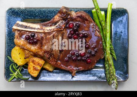 Gegrillter Knochen in Ribeye, serviert mit Kartoffeln und Sparragus, belegt mit einer frischen Huckleberry Portreduktion Stockfoto