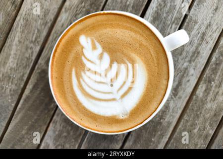 Weiße Tasse Kaffee mit Muster auf Schaumstoff, vor dem Hintergrund des Holztisches, Draufsicht Stockfoto