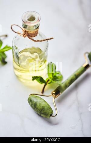 Flasche ätherisches Öl aus Minze und grünen Blättern und Jade-Massagerolle für das Gesicht. Natürliche Bio-Inhaltsstoffe für Kosmetika Stockfoto